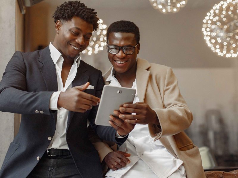 Black men in a cafe. Guy talking. Man in a black suit. Friends use the tablet.